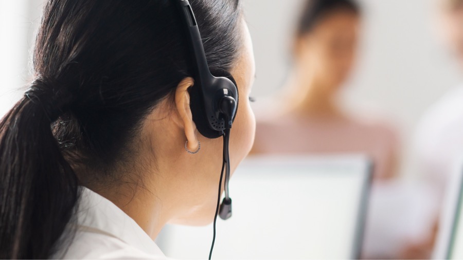 A woman wearing a headset and looking at a computer screen