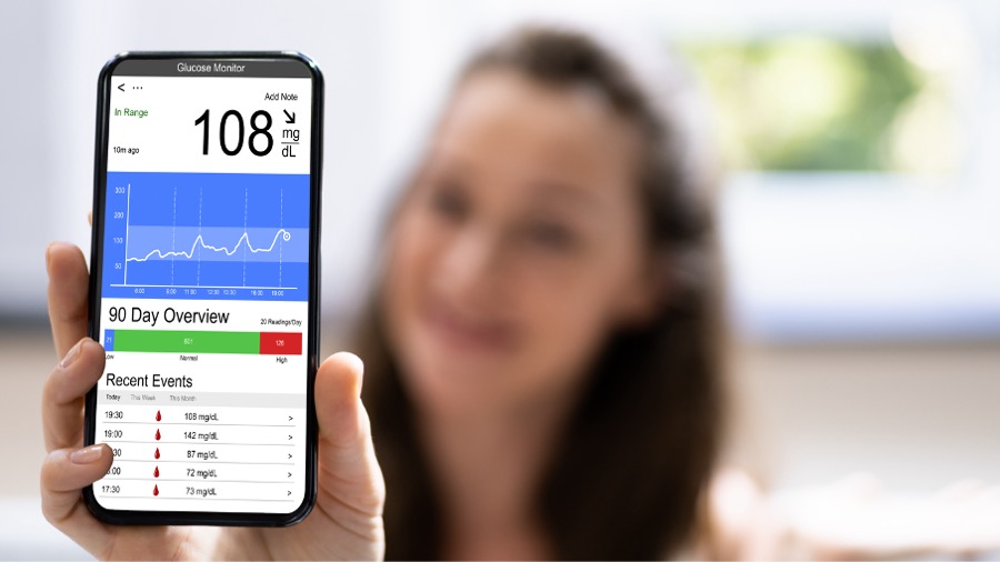 Woman holding smartphone displaying glucose monitoring app