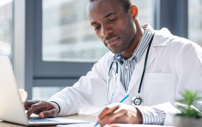 A doctor writing notes while using a laptop